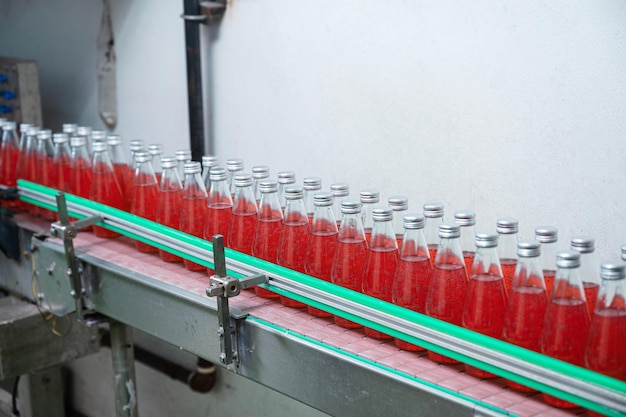 Glas gebotteld rood sap op stalen transportband van productielijn in drankverwerkingsfabriek