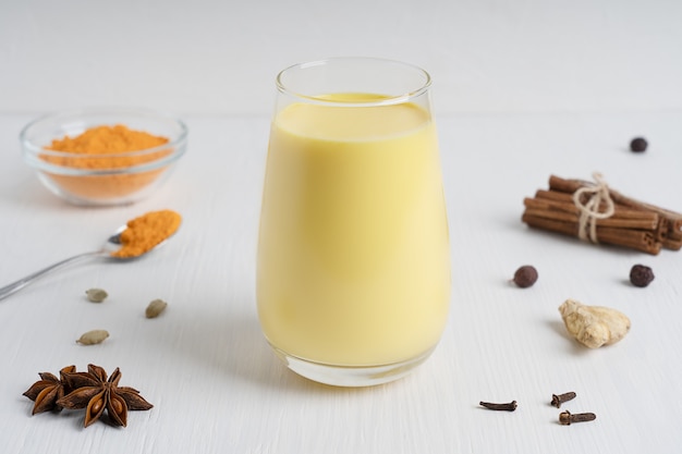 Glas goud of melk geserveerd met lepel kurkumapoeder, anijs en kruiden op witte houten tafel