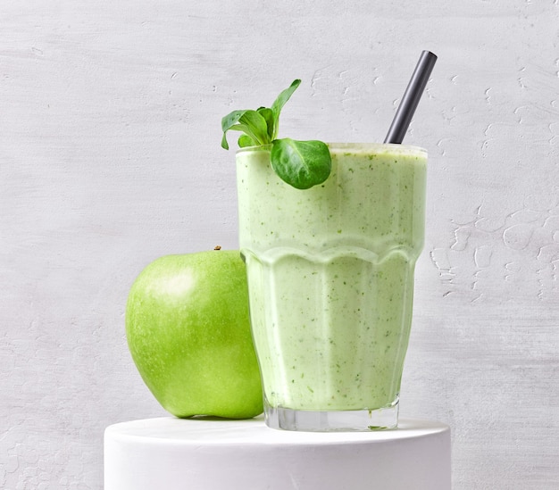 Glas groene smoothie en appel op witte standaard