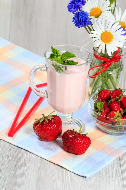 Glas heerlijke yoghurt met munt en verse aardbeien, kamille en korenbloemen in vaas op een houten tafel met een servet