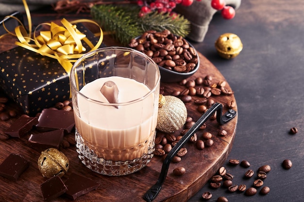 Glas Ierse room Baileys-likeur met ijs, gebrande koffiebonen, kaneel, kerstversiering en chocolade op donkere houten achtergrond. Kersttafel met cadeautjes. Selectieve aandacht.