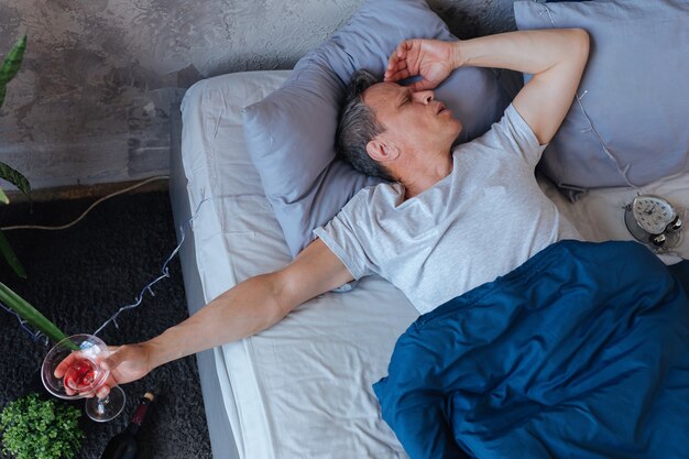 Glas in de hand. Slaperige volwassen man rusten op bed en glas te houden