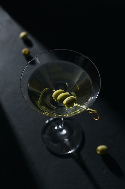 Glas klassieke droge martini cocktail met olijven op donkere stenen tafel tegen een zwarte achtergrond.