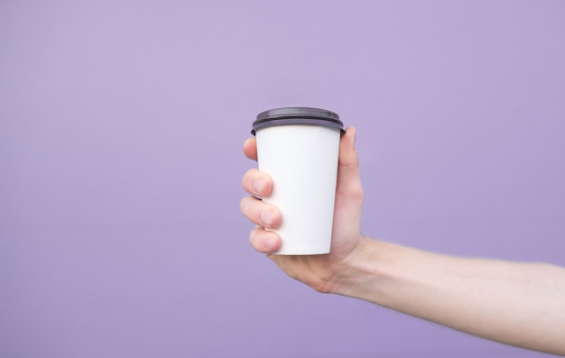 Glas koffie in de hand van een man op een pastel paarse achtergrond