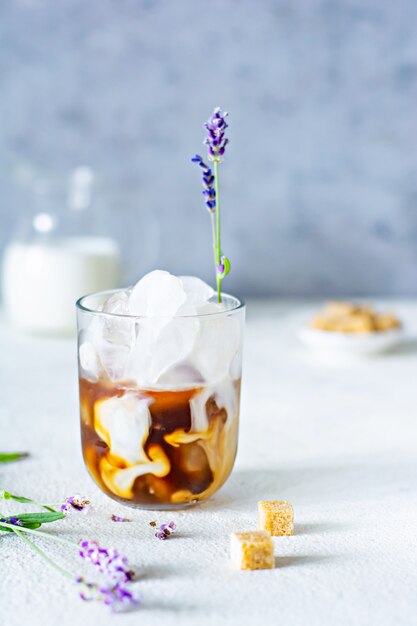 Glas koffie met ijs, melk en lavendel bloemen op een lichte achtergrond