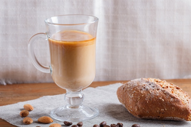 Glas kopje koffie met room en een broodje op een hout