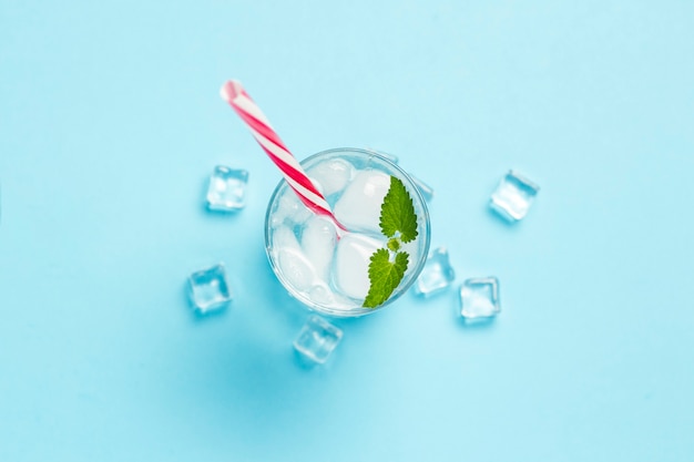 Glas koud en verfrissend water met ijs en munt op een blauwe achtergrond. Ijsblokje. Concept van hete zomer, alcohol, koel drankje, dorstlesser, bar. Plat lag, bovenaanzicht