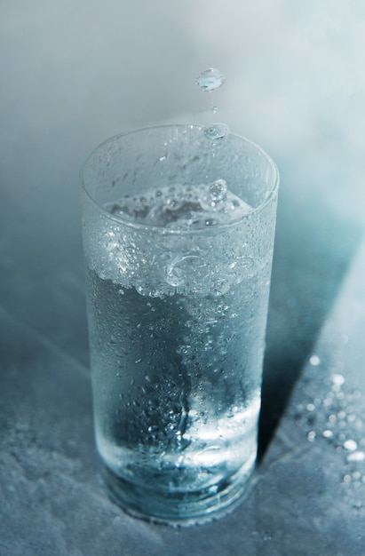 Foto glas koud helder water op een blauwe achtergrond met vallende druppels in een glas.