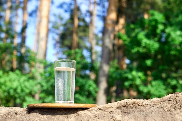 Glas koud water op een houten bord. Zand en bomen met aardachtergrond. Schoon waterconcept.