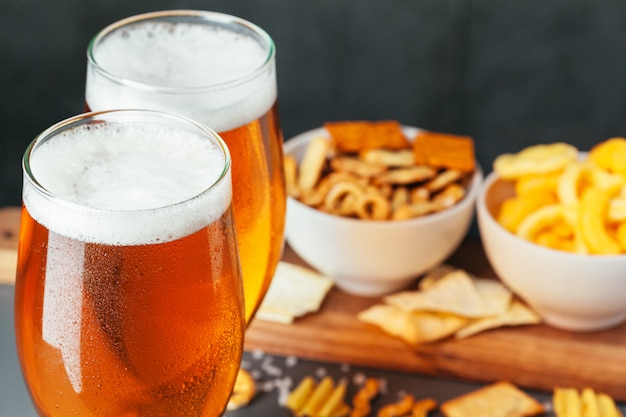 Glas lagerbier met snackkommen op donkere steenachtergrond