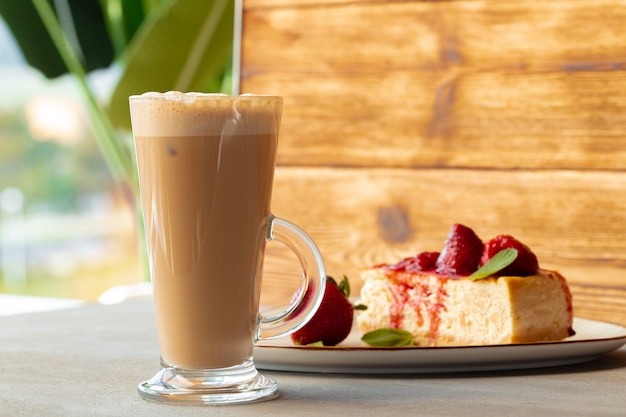 Glas latte koffie en stuk aardbeien cheesecake op grijze tafel