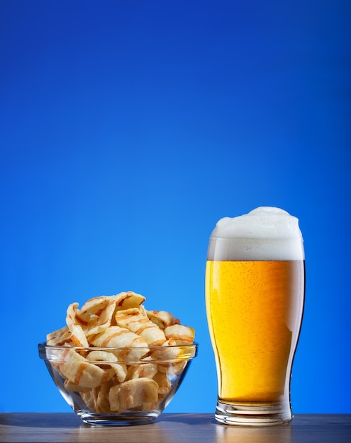 Glas licht bier en chips met spek op blauw