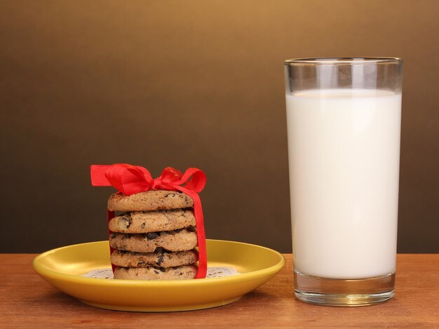 Glas melk en koekjes op houten tafel op bruine achtergrond