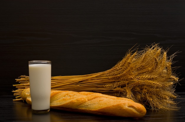 Glas melk en vers brood en een schoof op een zwarte achtergrond