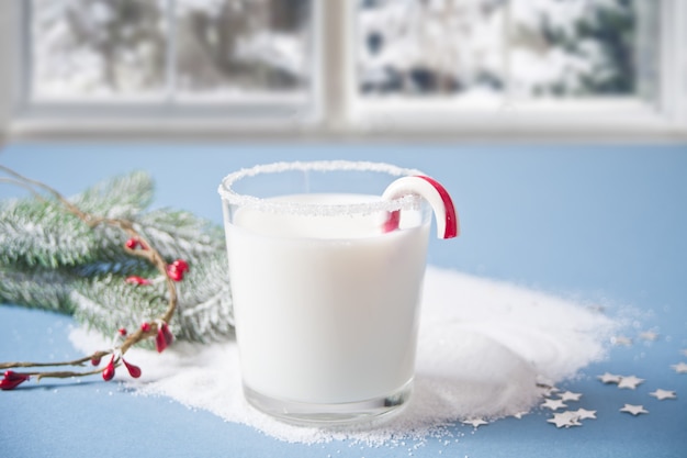 Glas melk, snoepgoed, kerstpijnboomtak op het blauwe nabijgelegen bevroren de wintervenster