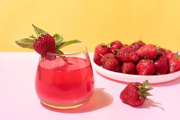 Glas met aardbeienlimonade en een bord aardbeien op gele en roze achtergrond in fel licht, zomerconcept, close-up.