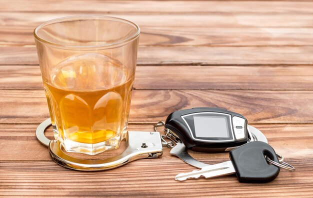 Glas met alcoholische drank handboeien en autosleutel op houten tafel