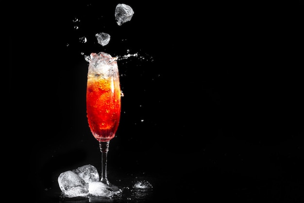 Glas met aperolcocktail op zwart ijs als achtergrond valt in het glas met de alcoholische drank