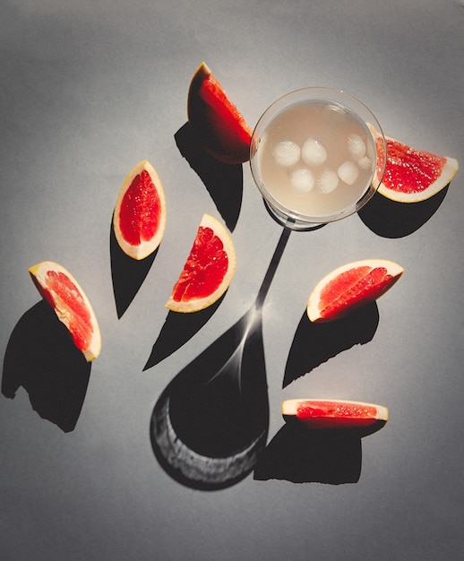 Glas met cocktail en gesneden grapefruits rond op grijs oppervlak.