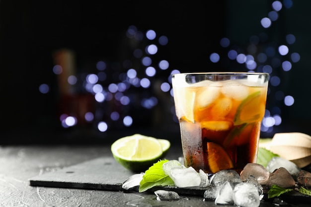 Glas met cola en limoen segmenten, juicer, ijs, munt tegen de achtergrond wazig licht