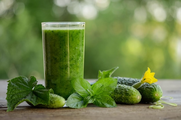 Glas met groene smoothie op een houten tafel en komkommers met bloemen en muntblaadjes