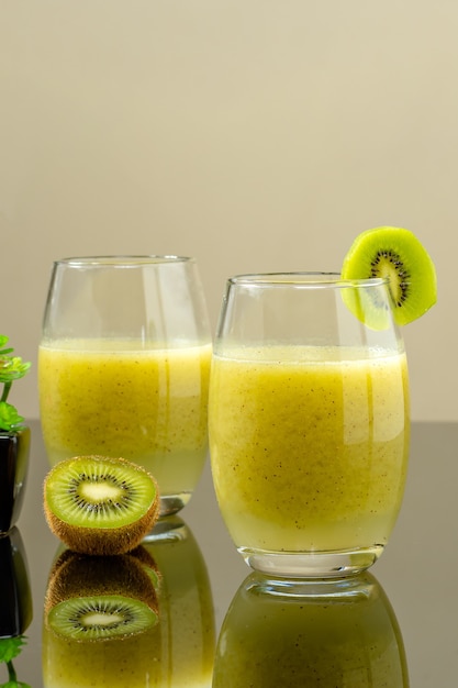 GLAS MET KIWI-SAP MET TWEE KIWI-HALVEN NAAST HET GLAS ONDER EEN REFLECTERENDE OPPERVLAKTE