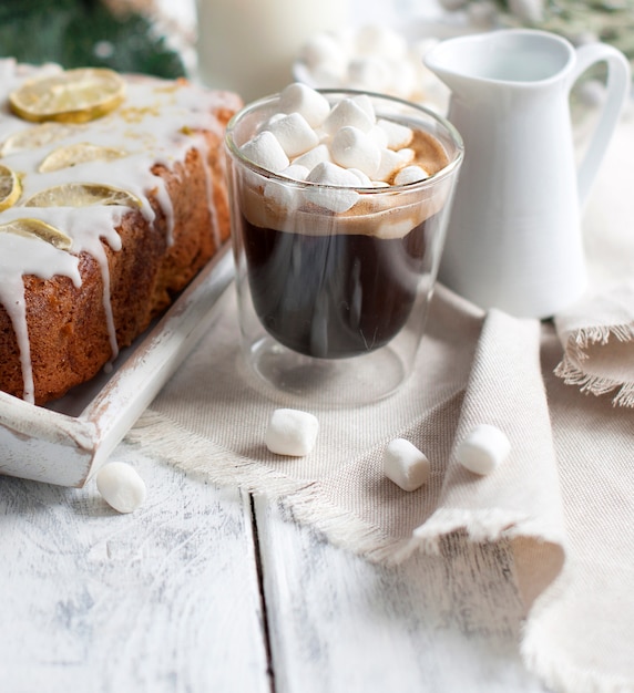 Glas met koffie en kleine marshmallows, citroencake en kerstboomtak