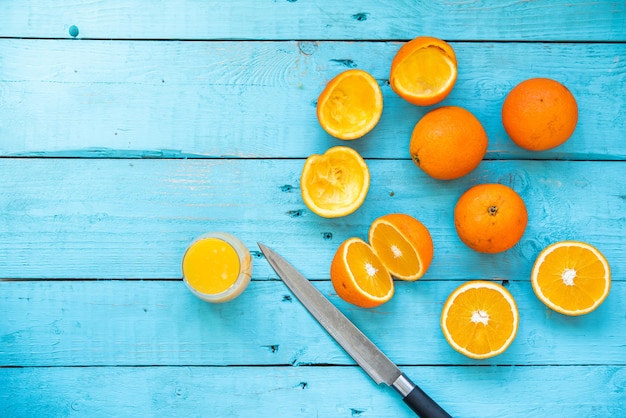 Glas natuurlijk sap van verschillende biologische sinaasappels, sommige heel, andere geperst, voor het dieet, op een blauwe houten tafel, met een mes ernaast. Gezond ontbijt