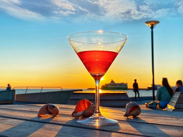 glas oranje water op strand houten tafelblad zeeschelp en avondrood