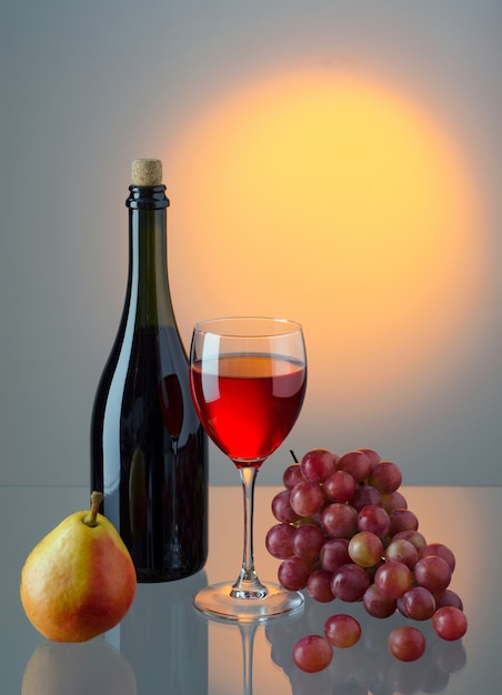 Glas rode wijn, fles wijn en fruit op felgekleurde achtergrond met kopieerruimte voor uw tekst.