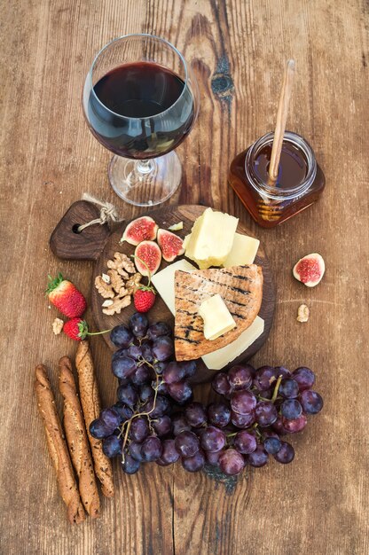 Glas rode wijn, kaasplank, druiven, vijgen, aardbeien, honing en brood sticks op rustieke houten tafel