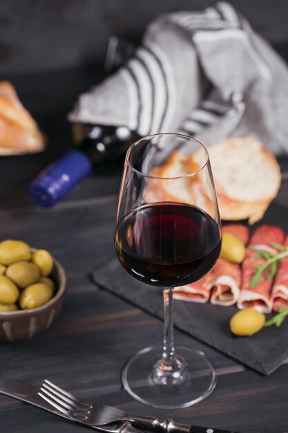Glas rode wijn met plakjes gezouten ham of Spaanse jamon serrano of Italiaanse prosciutto crudo brood groene olijven en rucola