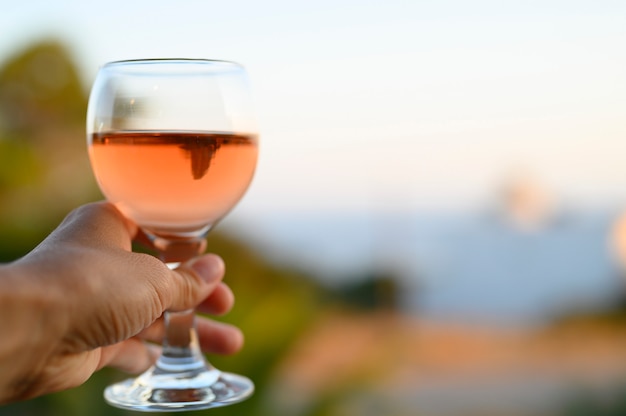 glas rose wijn in de hand van een vrouw tegen een wazig zeegezicht