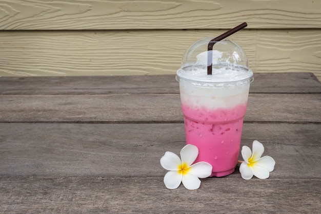 Glas roze ijsmelk dichtbij chite champaka op houten lijst in de koffiewinkel