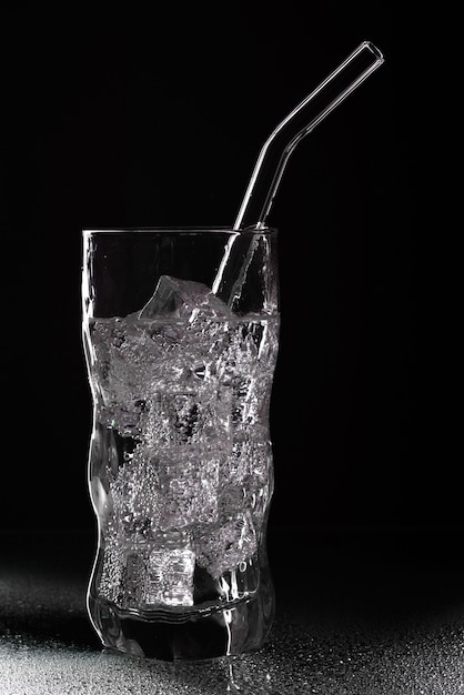 Glas sodawaterdrank met ijs op zwarte achtergrond. Gieten van helder water in glas op zwarte achtergrond
