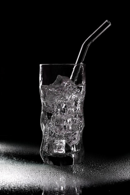 Glas sodawaterdrank met ijs op zwarte achtergrond. Gieten van helder water in glas op zwarte achtergrond