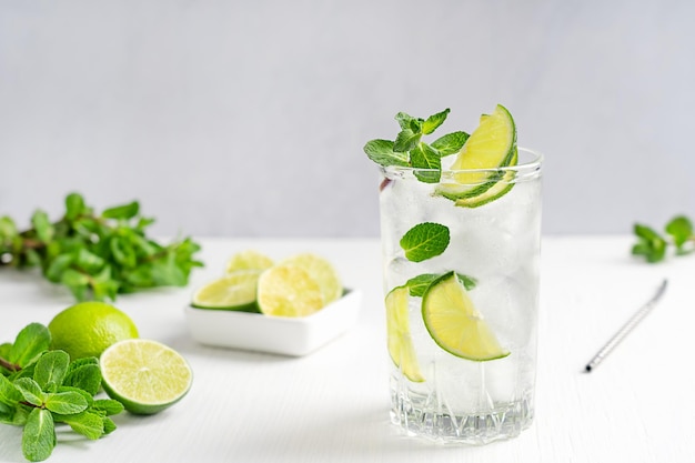 Glas verfrissende limonade met ijsblokjes geserveerd op houten tafel met schijfjes limoen en muntblaadjes