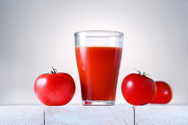 Glas vers organisch tomatesap met ruwe tomaten op lichte houten lijst.