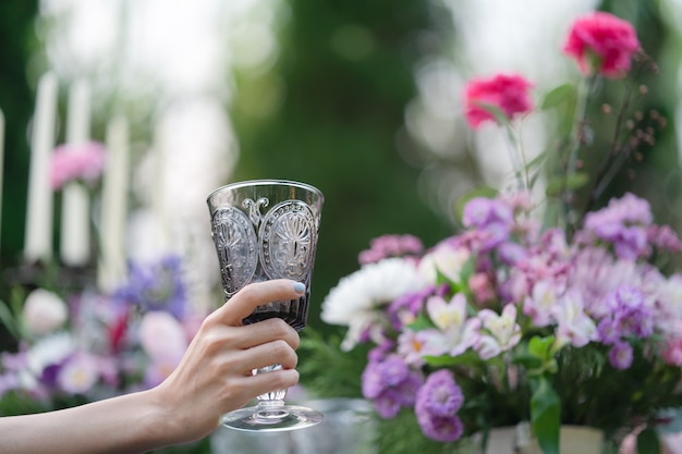 Glas water in vrouwenhand. Tuin en bloemen achtergrond.