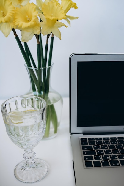 glas water met citroenlaptop en boeket gele bloemen op wit bureau