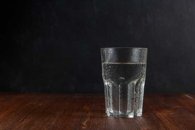 Glas water met waterdruppels op een houten tafel met donkere rug