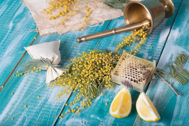 Glas water, mimosa bloemen, honingraat en stukjes citroen op een houten ondergrond. Detailopname