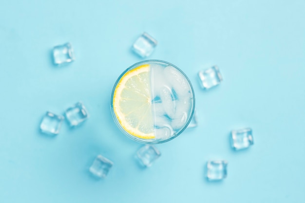 Glas water of drankje met ijs en citroen op een blauwe ondergrond met ijsblokjes. Concept van een hete zomer, alcohol, koel drankje, dorst lessen. Plat lag, bovenaanzicht