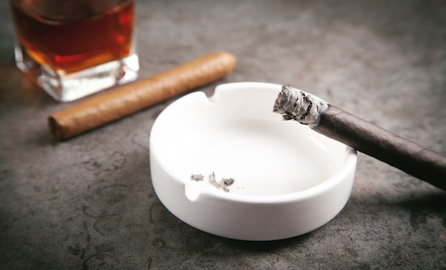 Glas whisky, asbak en sigaren op tafel.