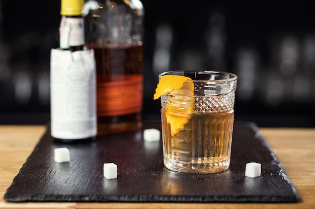 Glas whisky-cognac of cognac met citroen en ijsblokjes die op de toog staan met een fles op de achtergrond