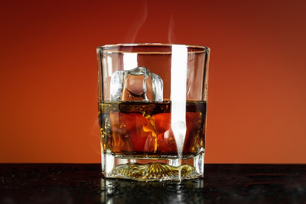 Glas whisky en ijsblokje op rood