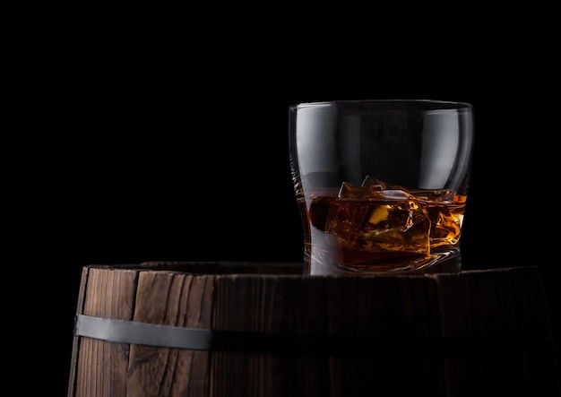 Glas whisky met ijsblokjes bovenop houten vat