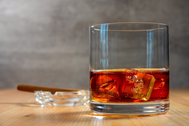 Glas whisky met ijsblokjes op de houten tafel. Een asbak met een sigaar in onscherpte