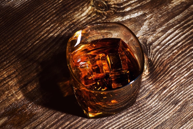 Glas whisky met ijsblokjes op houten tafel