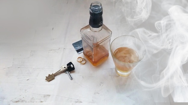 Glas whiskyfles en trouwringen in rook op grijze achtergrond